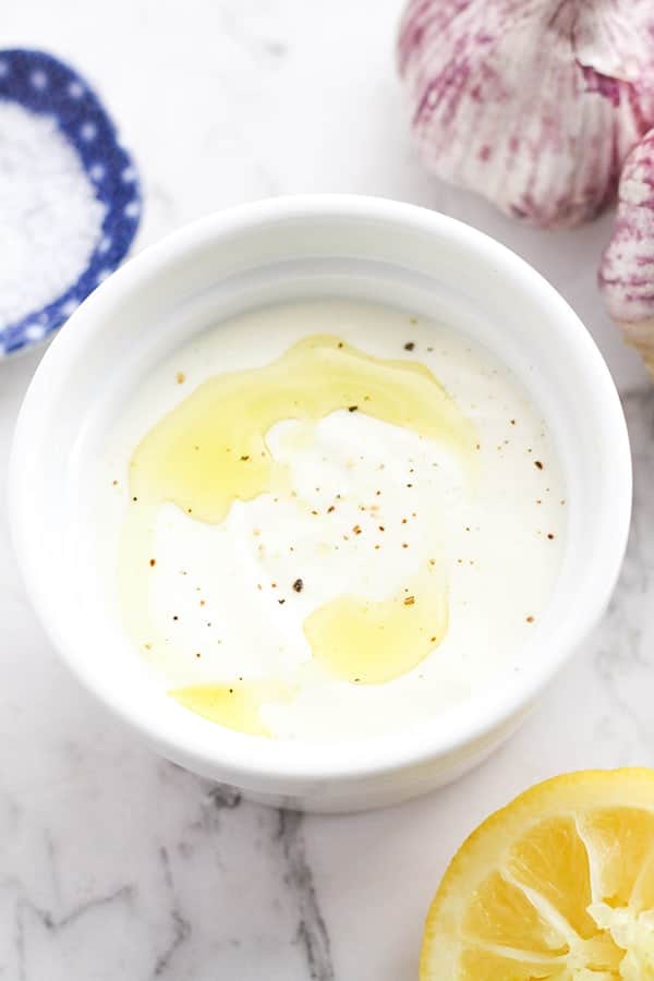 sauce in a white bowl surrounded by lemon, garlic and salt.