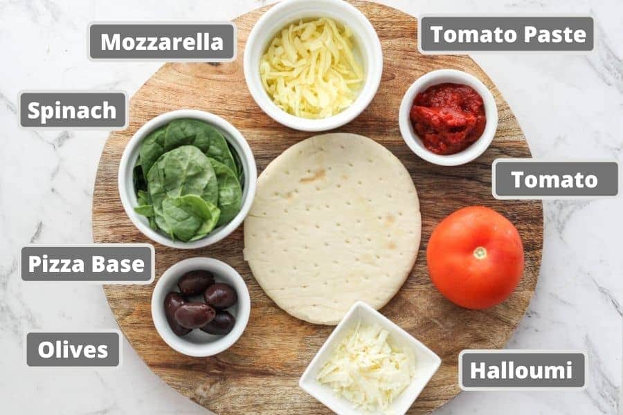ingredients for pizza on a wooden board including halloumi, tomato, spinach and olives.