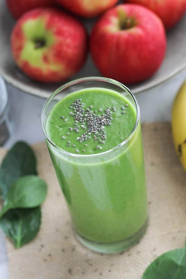 apple spinach smoothie in a tall glass topped with chia seeds.