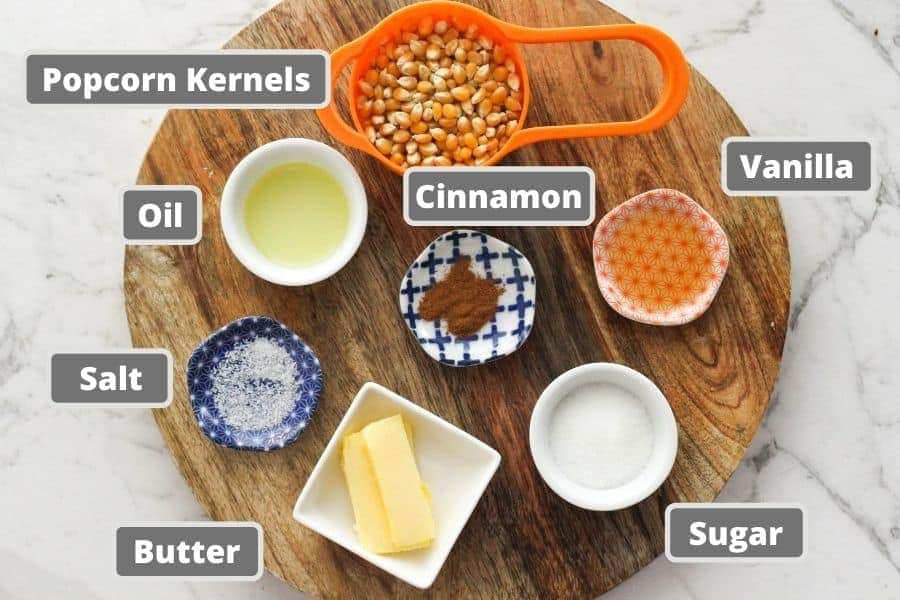 ingredients for cinnamon sugar on a wooden board including popcorn kernels, butter and sugar.