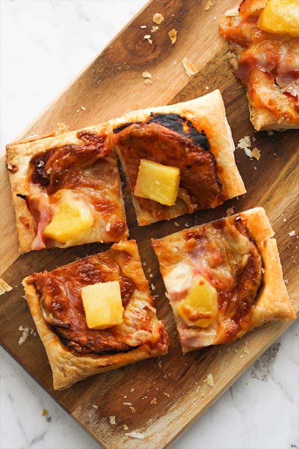 slices of Hawaiian pizza on a wooden serving board.