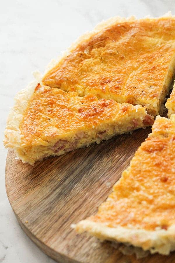 bacon and egg pie sliced on a wooden board with a piece missing.