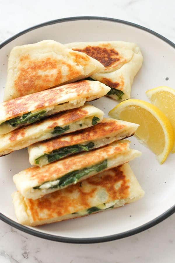 spinach and feta gozleme stacked on top of each other on a white plate.