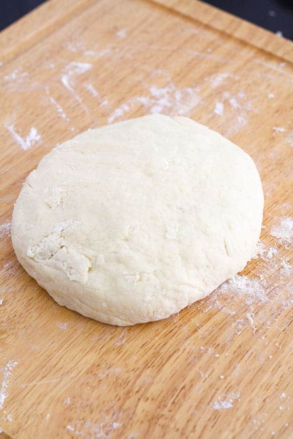 scone dough in a large disc shape on a wooden board.