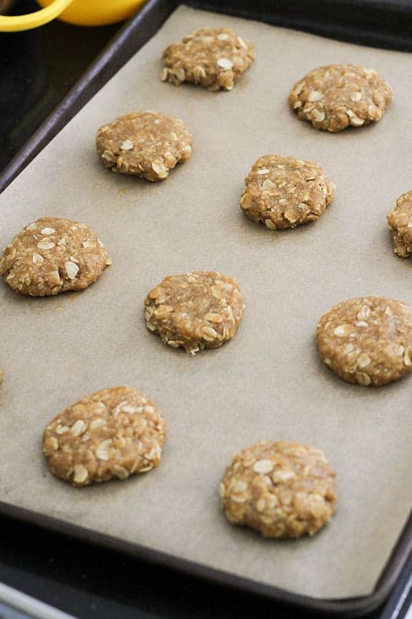 uncooked anzac biscuits on a baking tray.