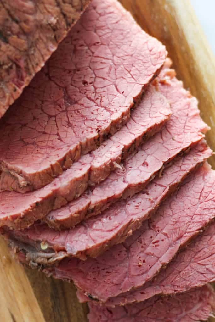 slices of corned beef on a wooden serving board.