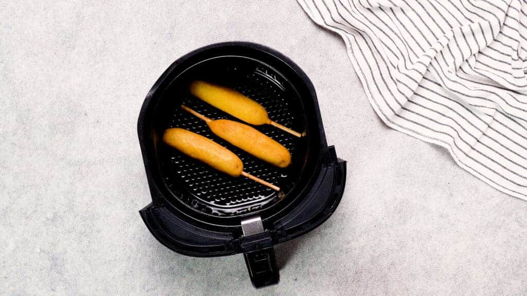 top shot of air fryer basket with prepared frozen corn dogs in it