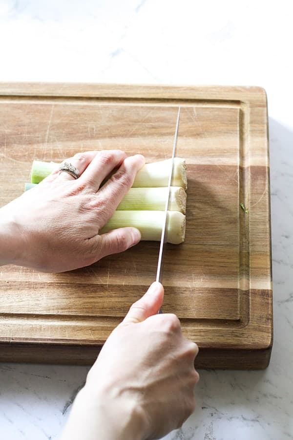 Leeks on a wooden chopping board with a hand cutting the root ends off.