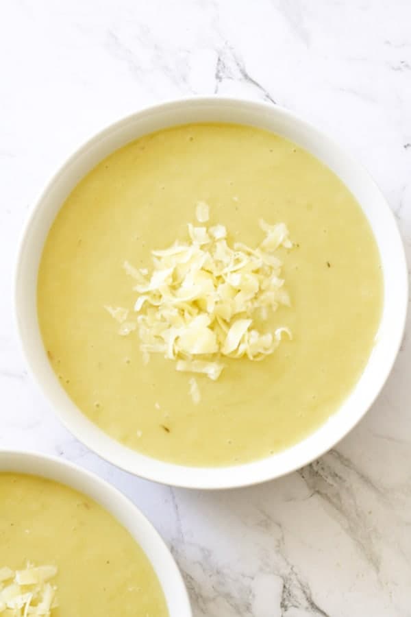 Potato and Leek Soup in a white bowl topped with shredded cheddar cheese.