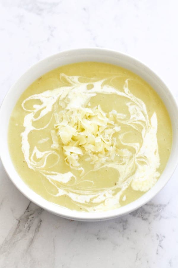 Potato and Leek Soup in a white bowl covered in heavy cream swirls.