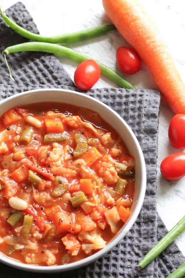 cannellini bean soup in a white bowl surrounded by tomatoes, carrots and beans