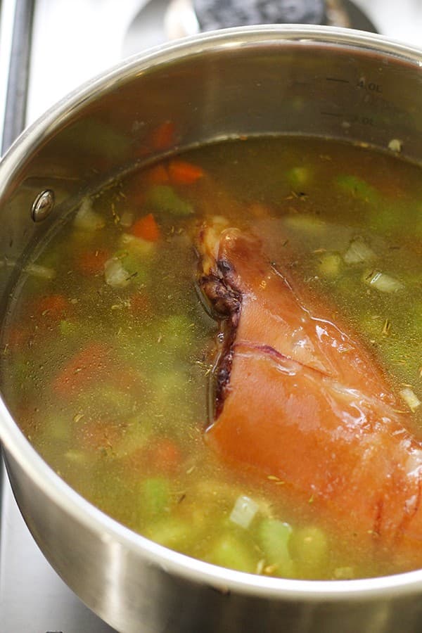 Split pea soup ingredients and a ham hock in a saucepan. 