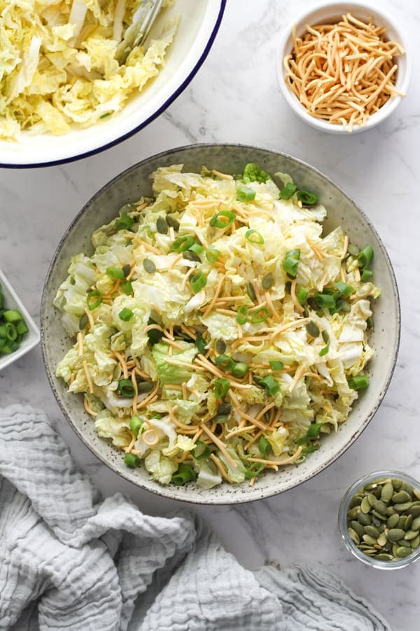 salad in a large bowl surrounded by small bowls of pepitas, noodles and green onions.