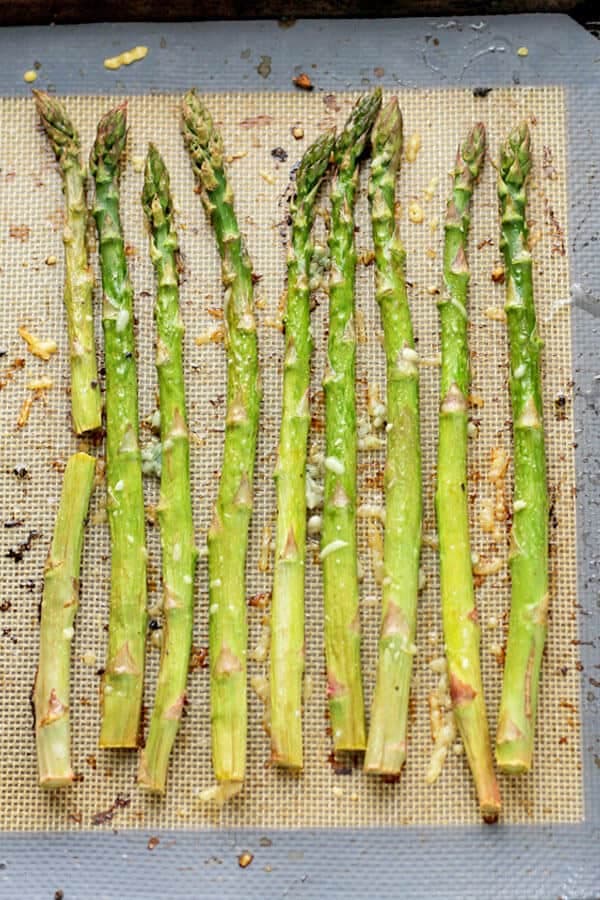 cooked asparagus spears laid out in a single layer on a baking tray covered in parmesan cheese and minced garlic