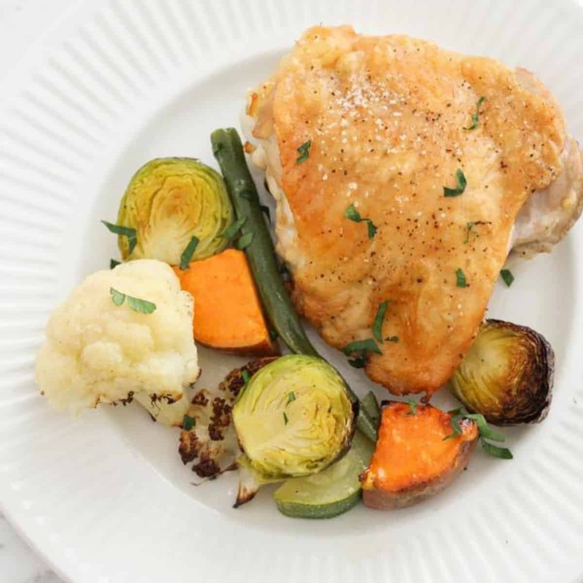 crispy baked chicken thigh and vegetables on a white plate.