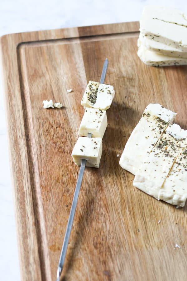 uncooked cubes of halloumi on a metal skewer.
