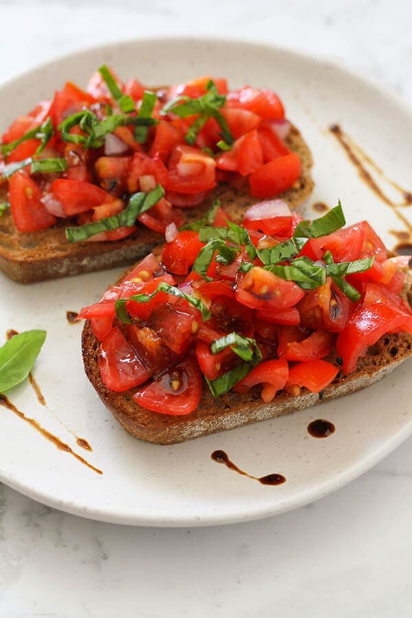 two pieces of brushetta on a white plate covered in balsamic glaze.