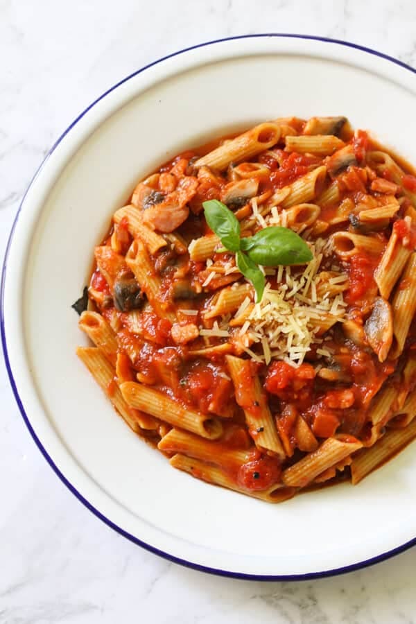bacon and mushroom pasta on a white plate with basil and parmesan cheese on top.