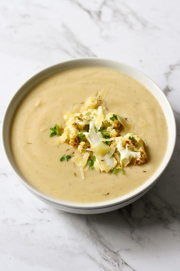 a bowl of cauliflower soup with roasted cauliflower, shredded cheese and parsley on top.