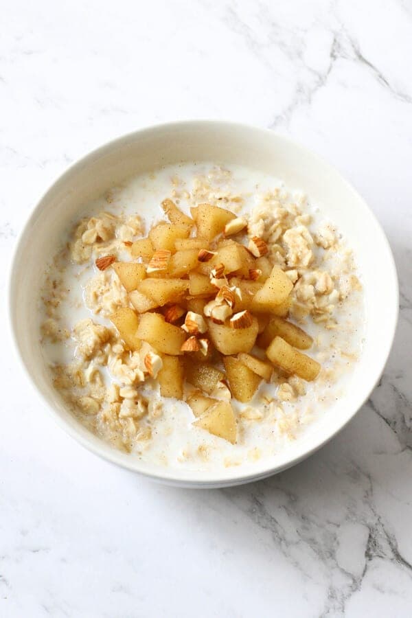 a bowl of oatmeal topped with stewed apple and almonds.