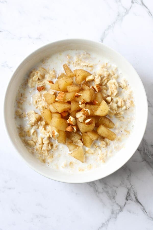 a bowl of oatmeal topped with stewed apple and almonds.