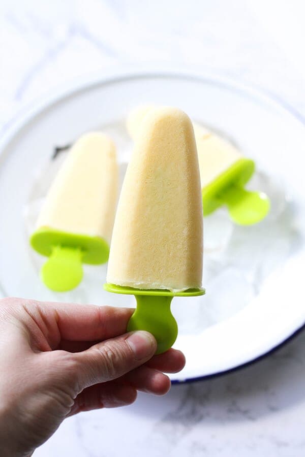 a hand holding a mango popsicle.