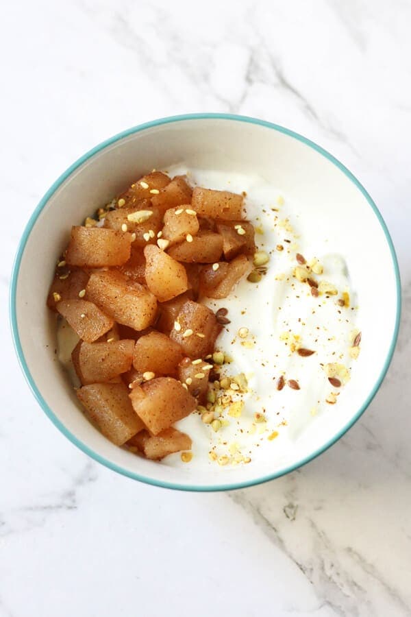 stewed cinnamon apples on top of greek yoghurt in a white bowl.