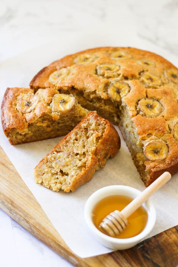 banana cake on a wooden board with a small bowl of honey.