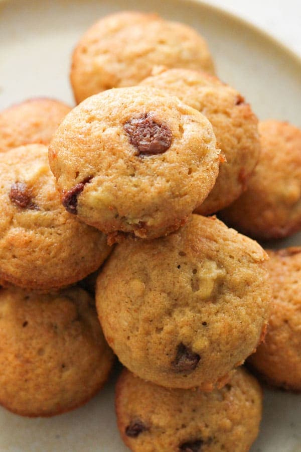 mini banana and choc chip muffins stacked on a plate.