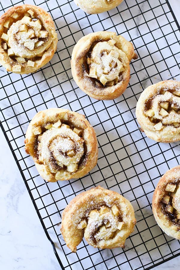 apple and cinnamon scrolls sitting on a cooling rack. 