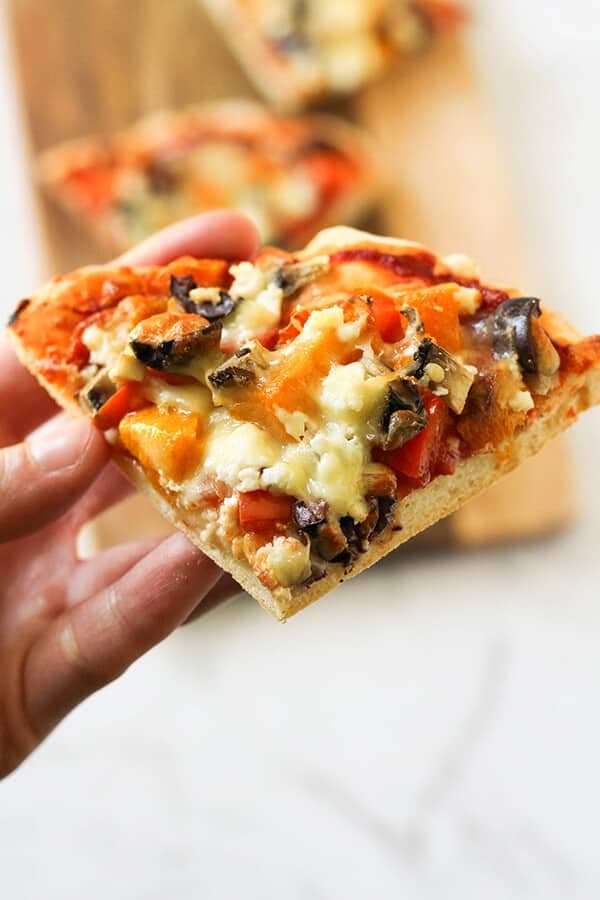 A hand holding a slice of Roast Pumpkin Pizza.