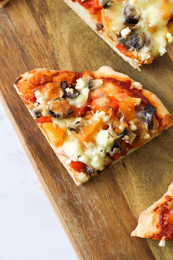 A slice of Roast Pumpkin Pizza on a wooden serving board.