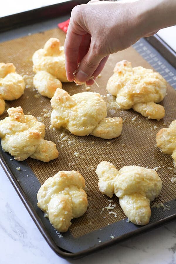 garlic knots on a baking tray being sprinkled with parmesan cheese.