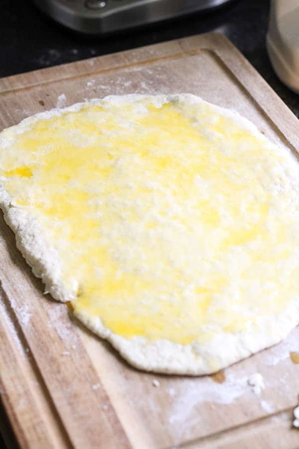 dough rolled out on a wooden board covered in butter.