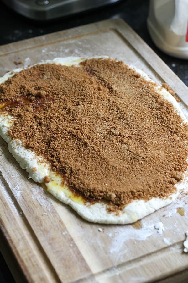 dough rolled out on a wooden board covered in cinnamon sugar.
