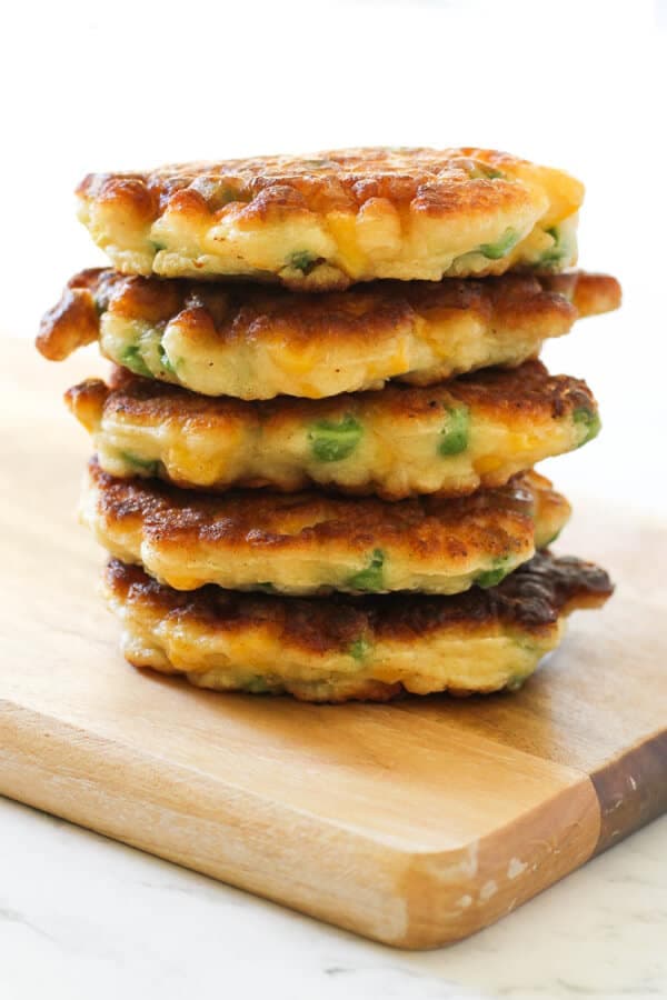 Pea & Sweet Corn Fritters stacked on top of each other on a wooden board.