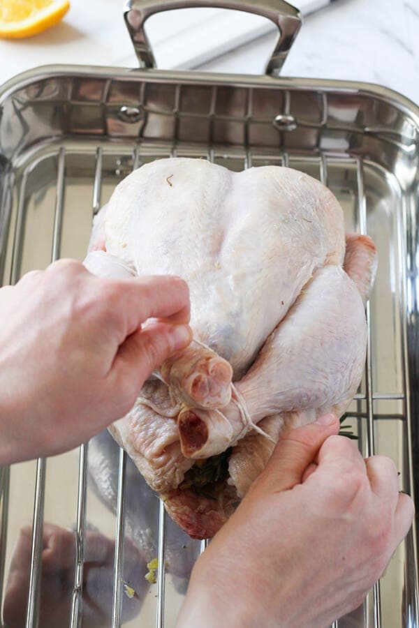 Hand tying the legs of a whole chicken together.