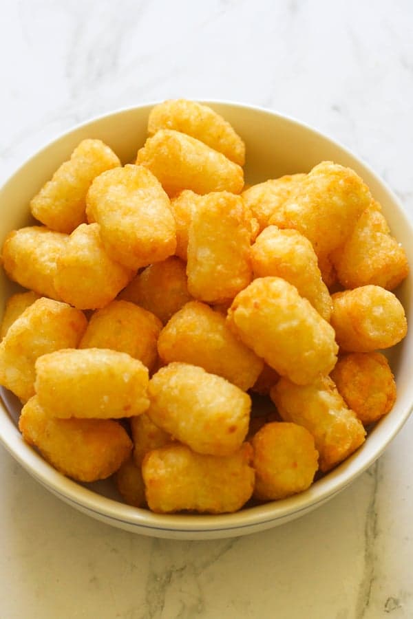 A white bowl filled with crispy tater tots.
