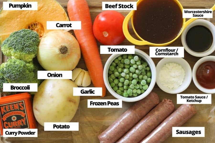 ingredients for curried sausages laid on top of a wooden cutting board.