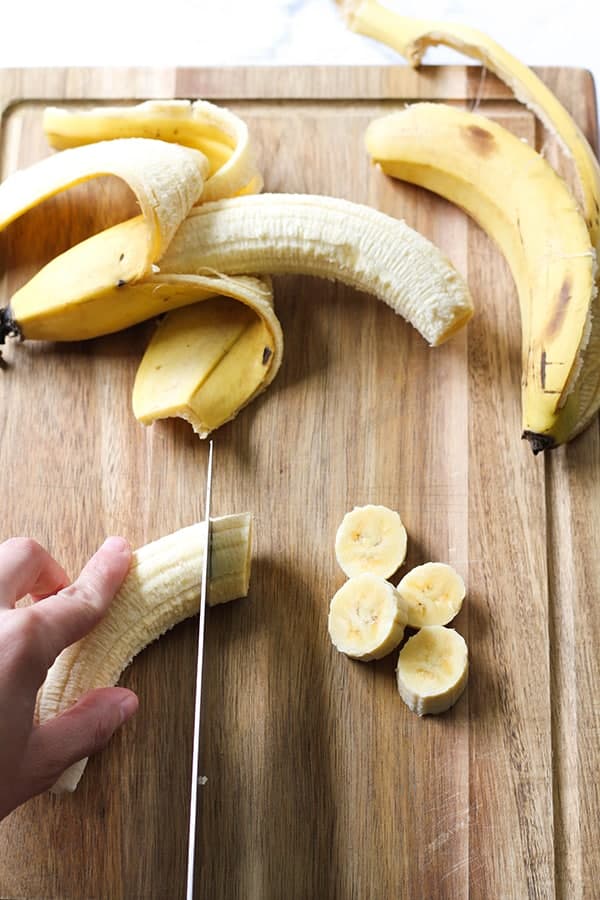banana being sliced on a wooden cutting board.