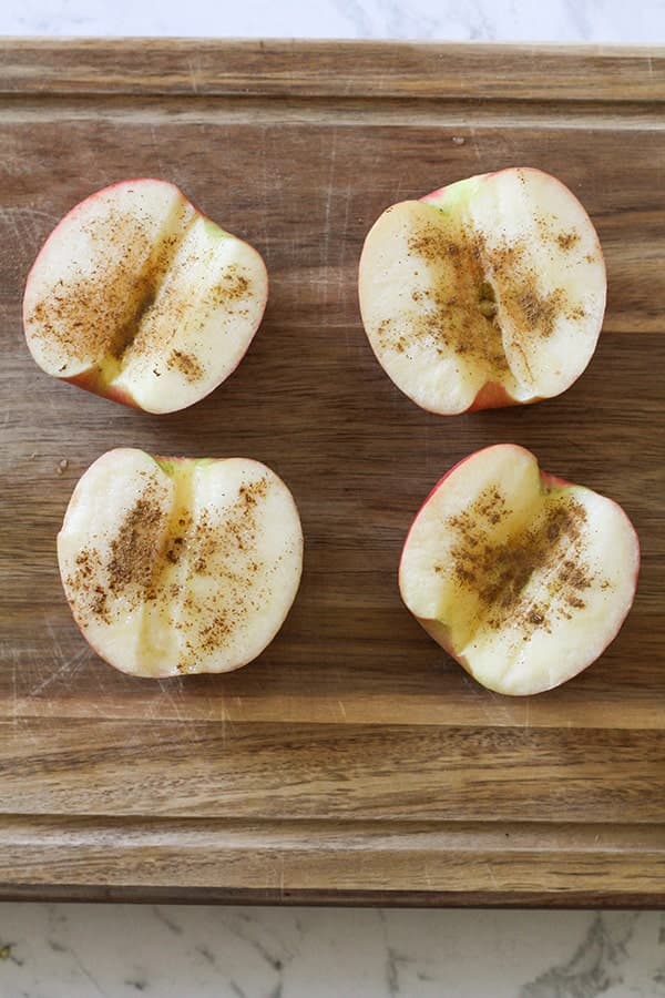 apple halves covered in cinnamon on a wooden board.