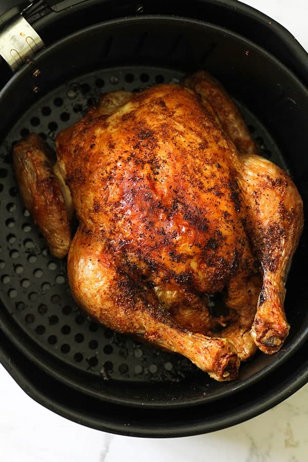 Whole roast chicken sitting in air fryer basket.