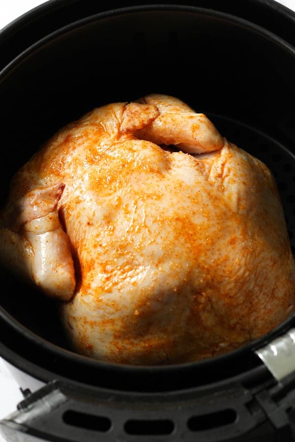 chicken sitting in air fryer basket ready to be roasted.