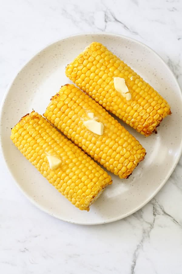3 corn on the cob on a white plate. 