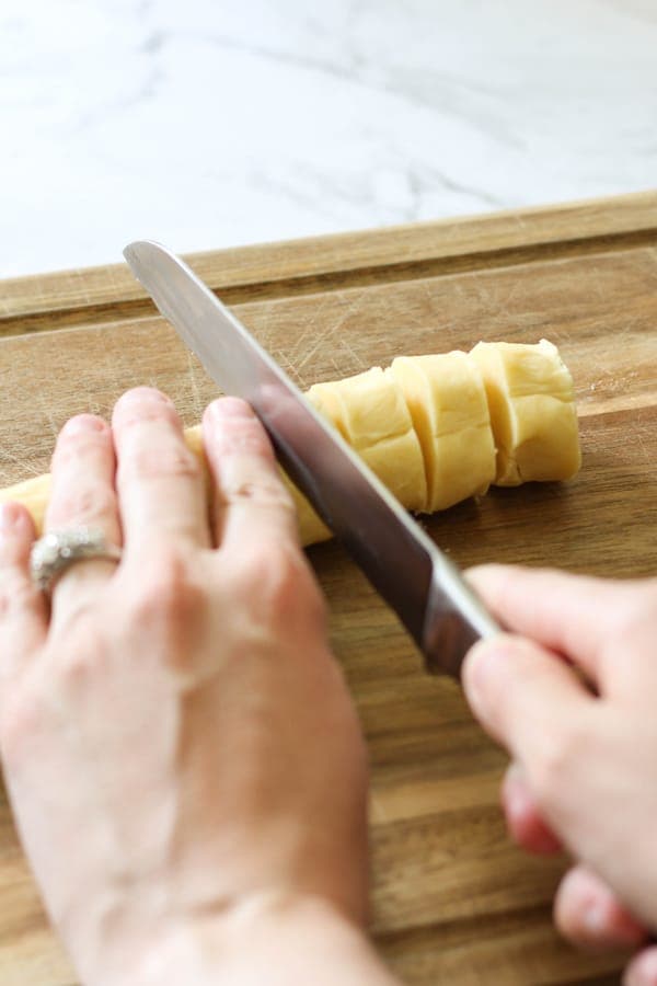 a hand slicing a shortbread dough log into round to be baked.