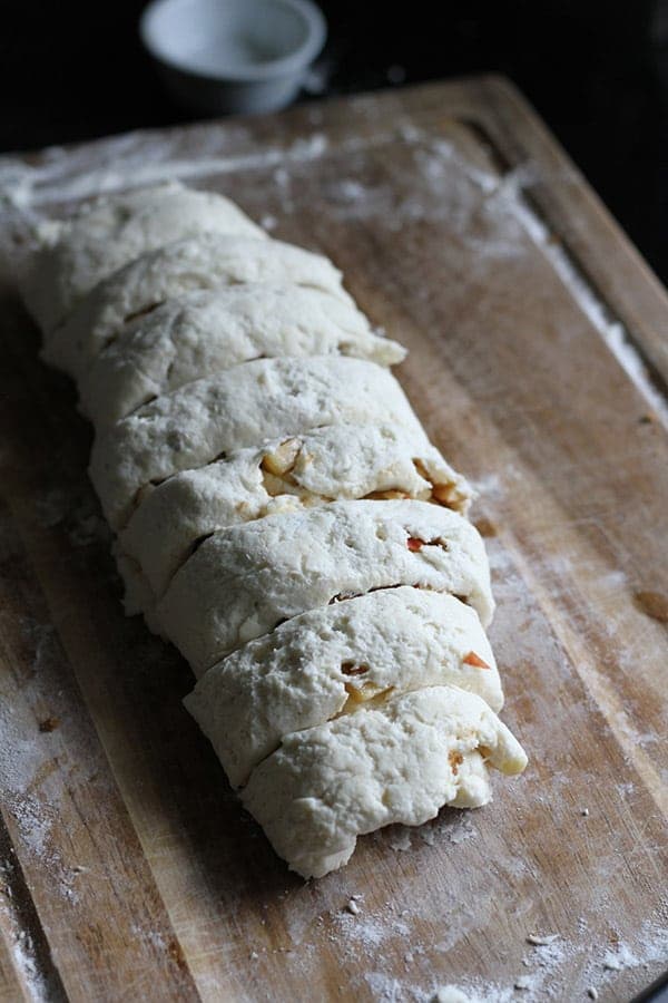 apple cinnamon rolls being cut on a wooden board.