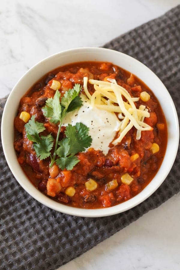 vegetarian three bean chili in a white bowl topped with greek yoghurt, cheese and cilantro.