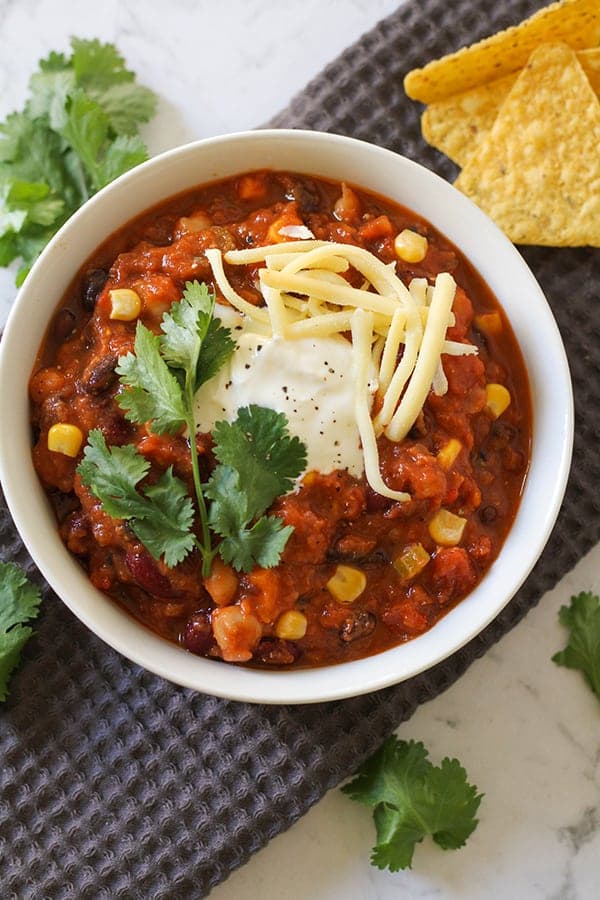 vegetarian three bean chili in a white bowl topped with greek yoghurt, cheese and cilantro.