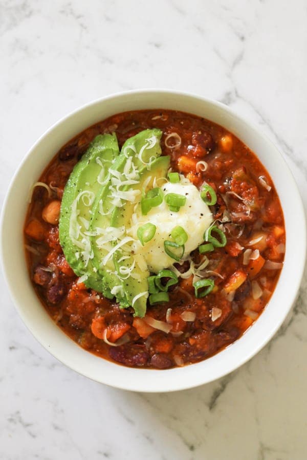 vegetarian three bean chili in a white bowl topped with greek yoghurt, avocado and spring onions.
