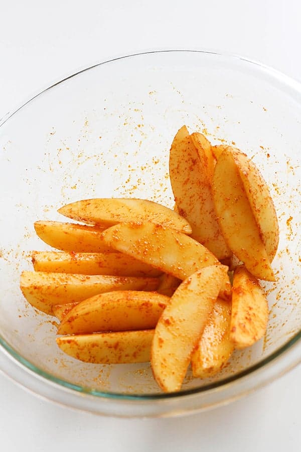 potatoes covered in seasoning in a glass bowl.